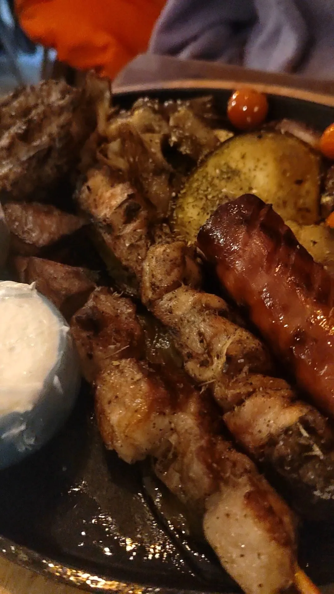 Grilled meat skewers and a sausage on a dark plate with a lemon wedge