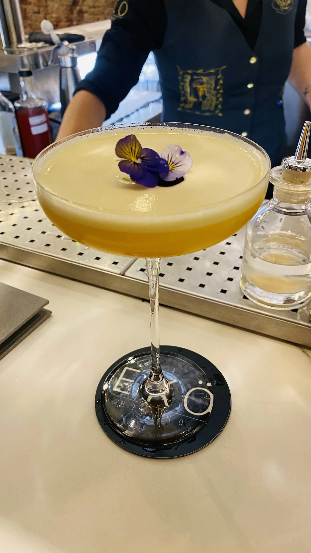 A yellow cocktail garnished with a small flower in a coupe glass