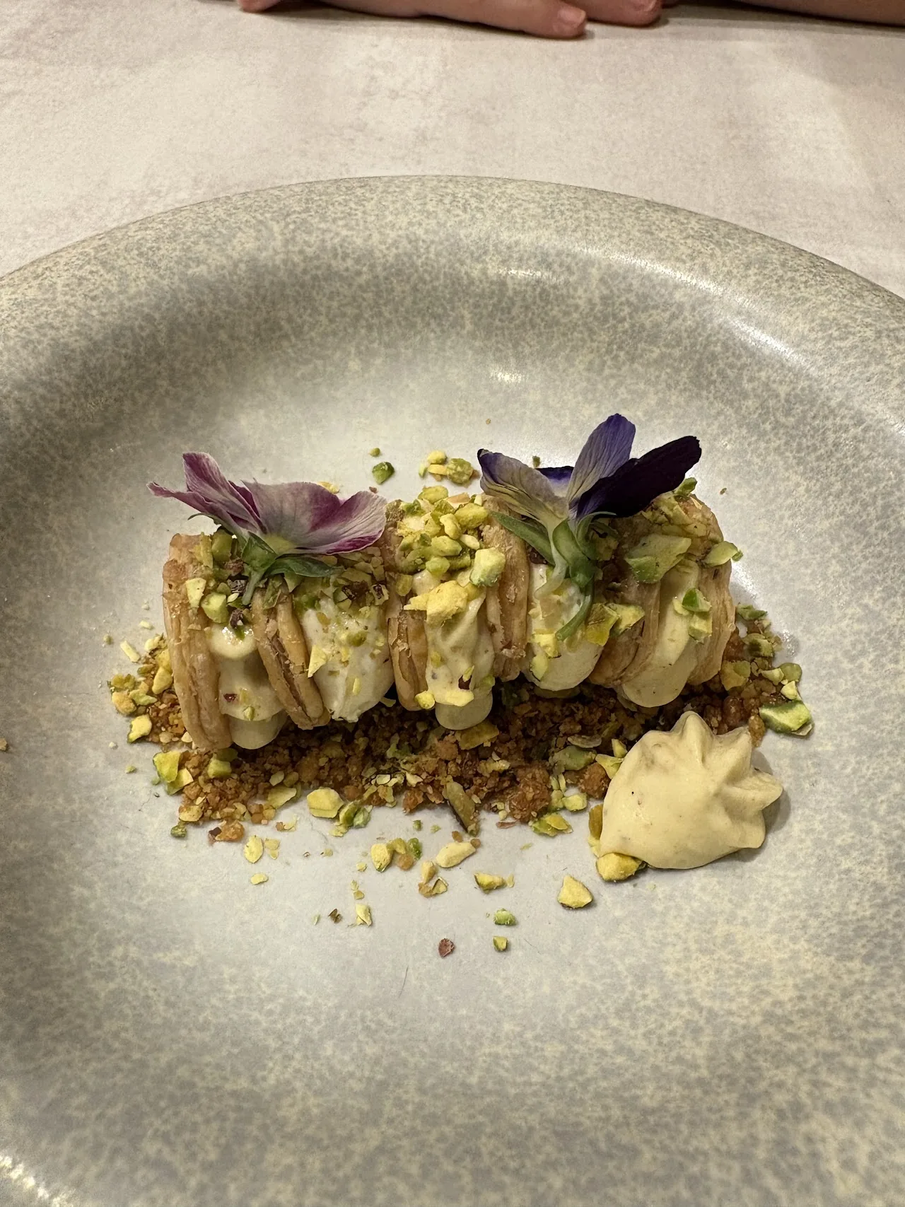 A dish with a pistachio crumble, herbs, and a swirl of sauce on a plate