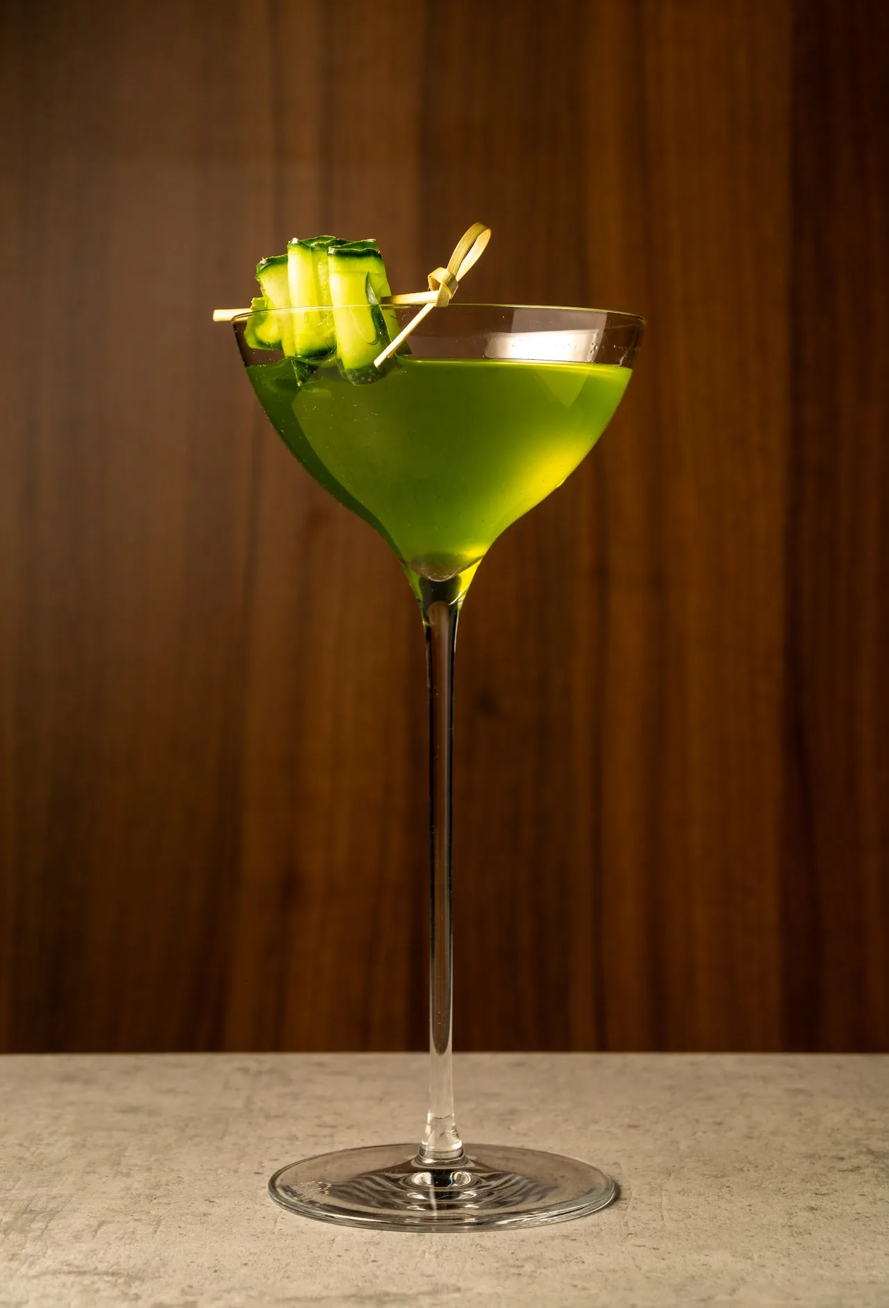 A green cocktail garnished with cucumber in a martini glass