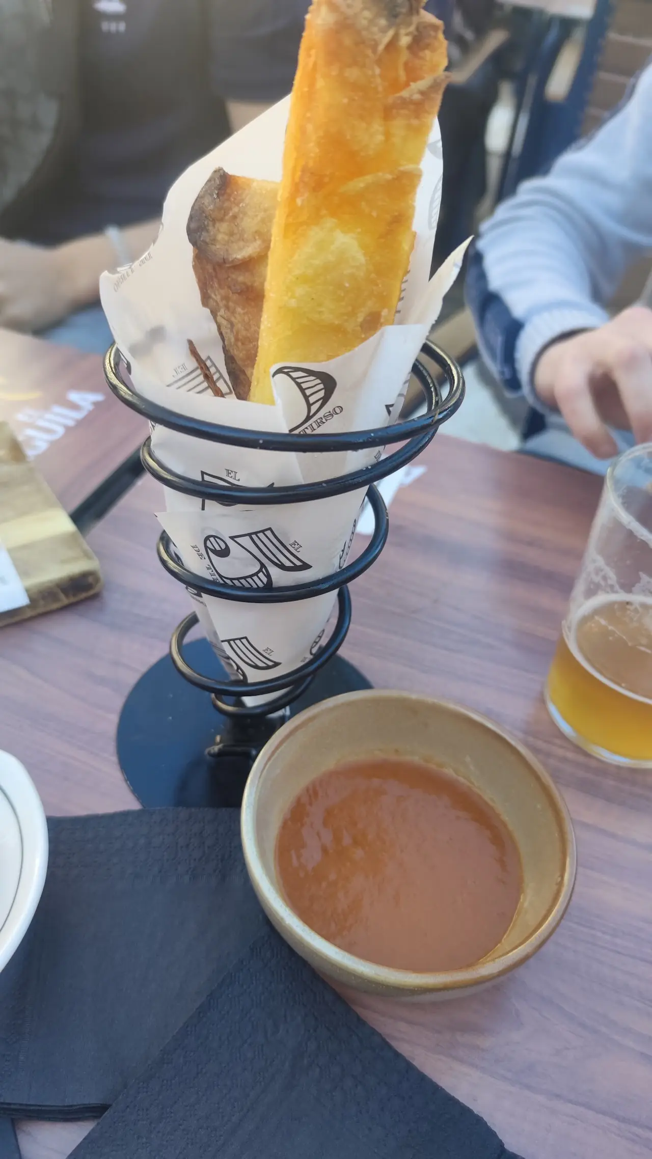 Churros in a paper cone beside a cup of hot chocolate