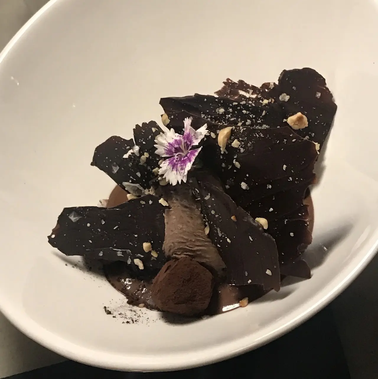 Chocolate dessert with hazelnuts and an edible flower on a white plate, at El 58.
