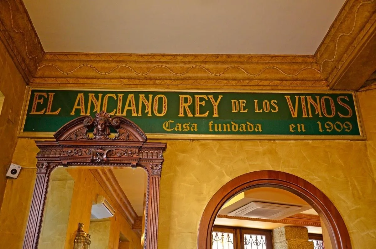 A green painted wall sign with gold lettering above an ornate carved wooden mirror frame and an arched doorway.