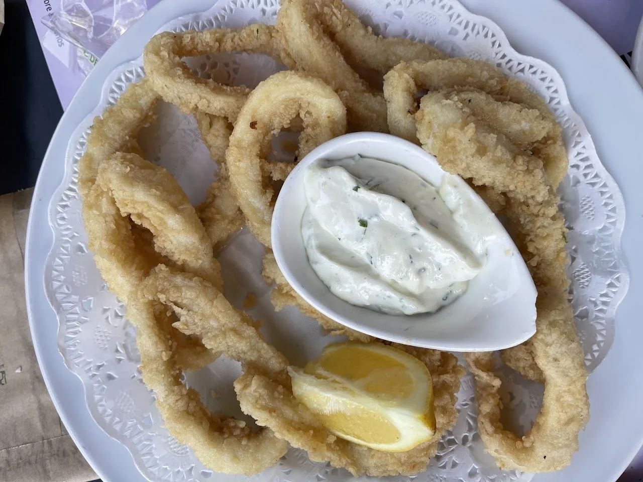 A plate of fried squid rings with a small dish of white sauce and a lemon wedge