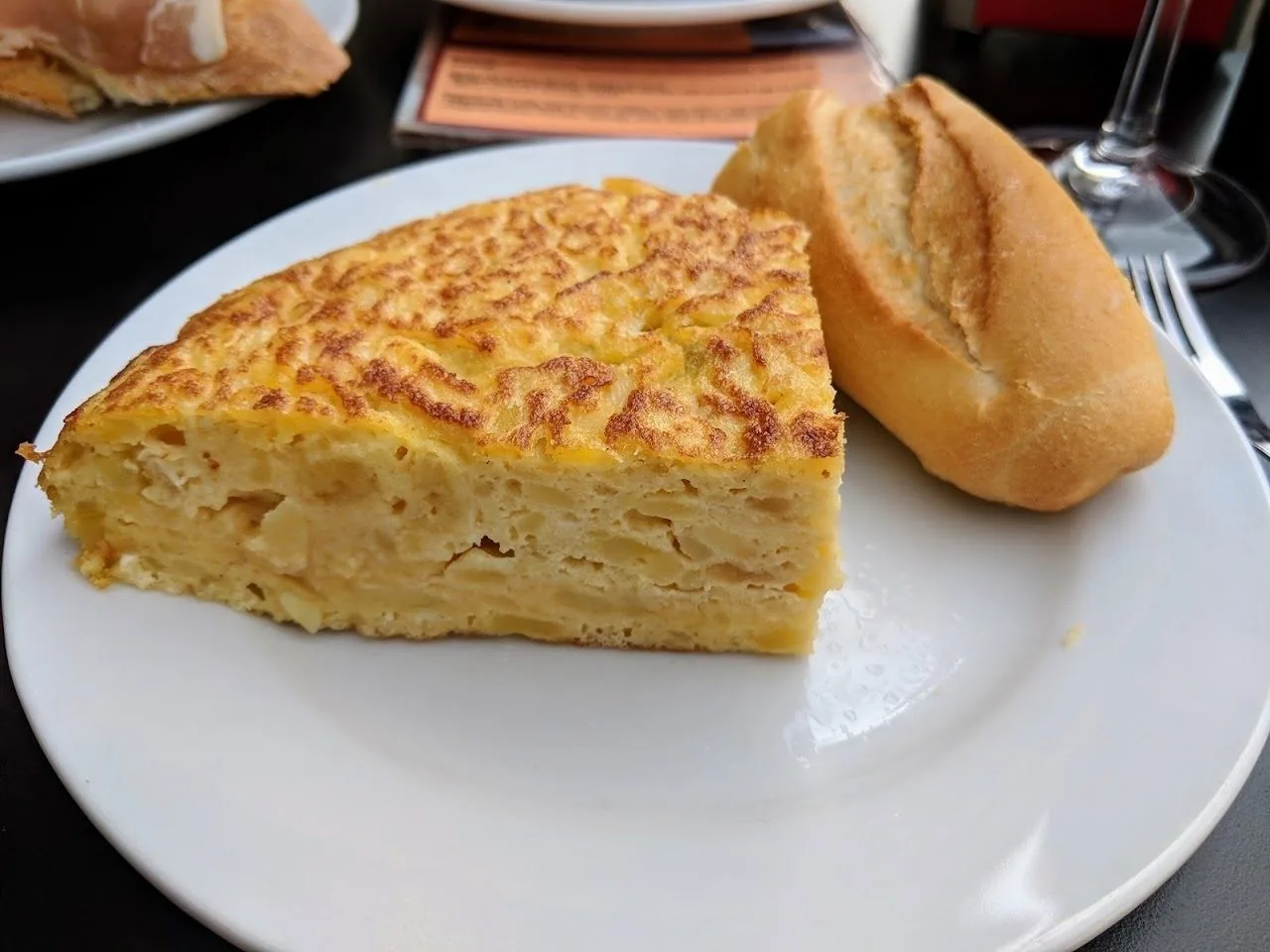 A wedge of Spanish omelette and a bread roll on a white plate