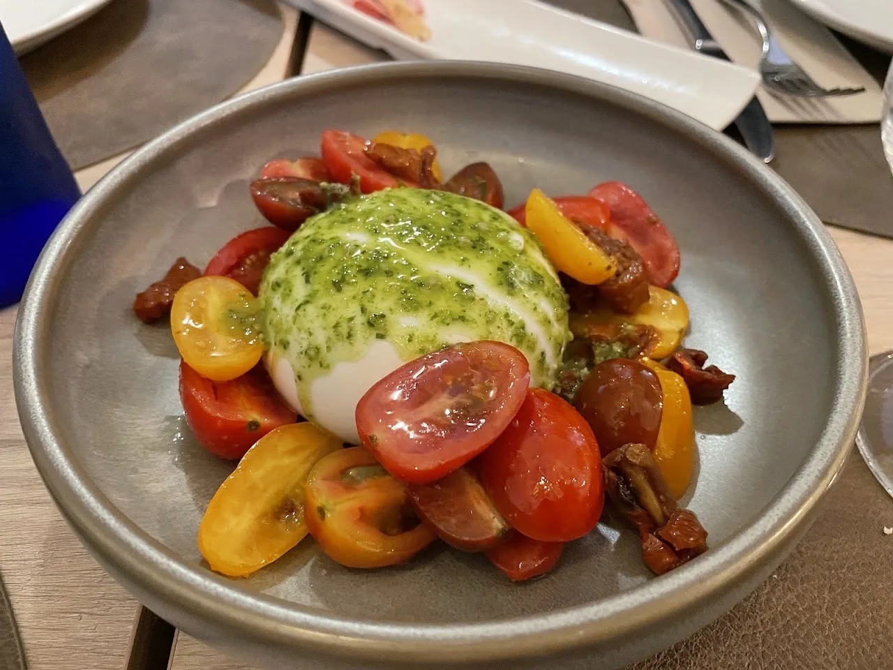A grey bowl of burrata with cherry tomatoes and green pesto