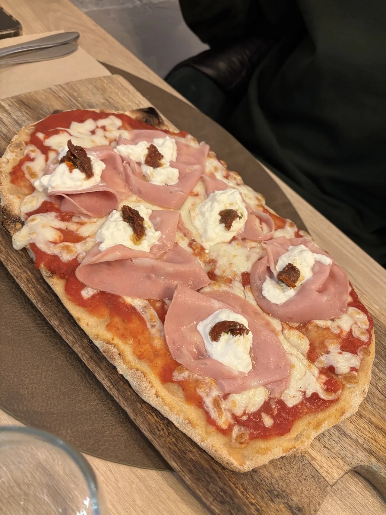 A long flatbread topped with ham and dollops of cream cheese on a wooden board