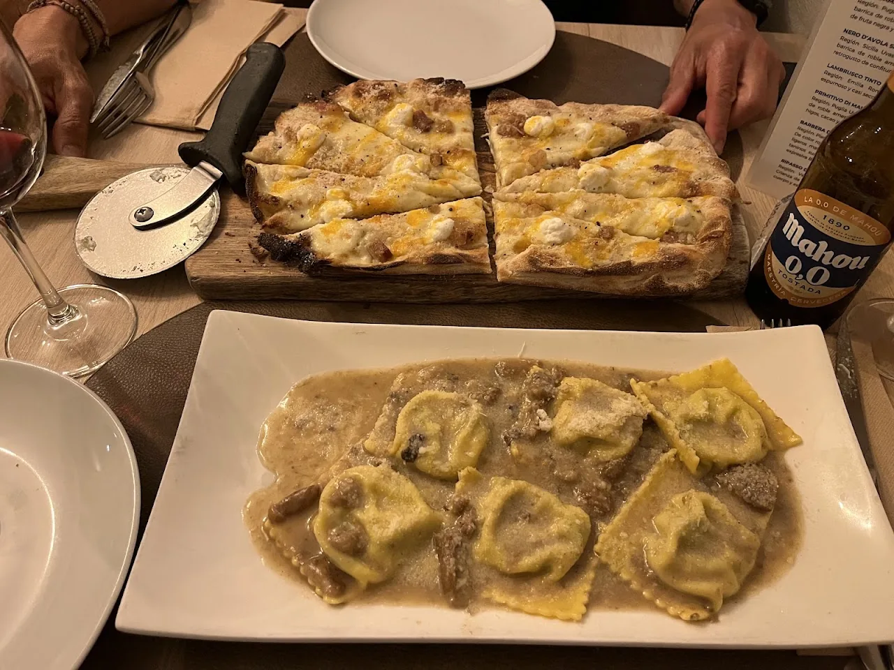 A tray of ravioli in cream sauce alongside sliced flatbread pizza