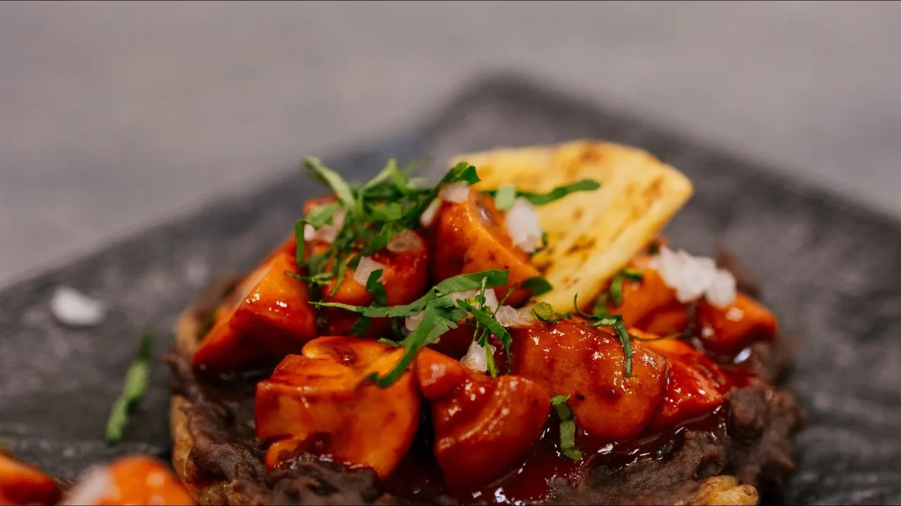 A small tortilla base topped with diced orange sauce-coated pieces, herbs and a tortilla chip