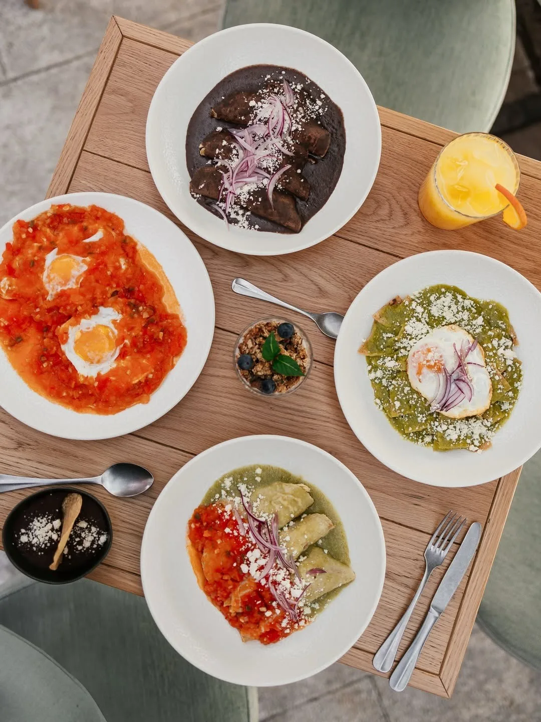 An overhead view of plates of eggs in red and green sauce and a dark sauce with onion on a wooden table