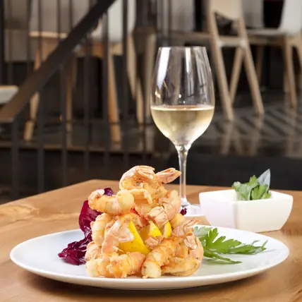 Plate of battered fried prawns with lemon and a glass of white wine on a wooden table