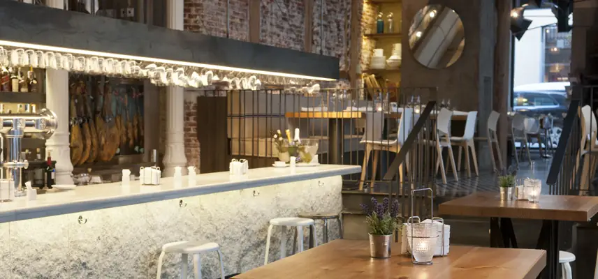 Restaurant interior with a marble bar, hanging jamon legs, wooden tables and exposed brick walls