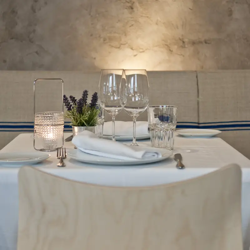 Set table with wine glasses, a candle lantern and lavender against a plaster wall and banquette