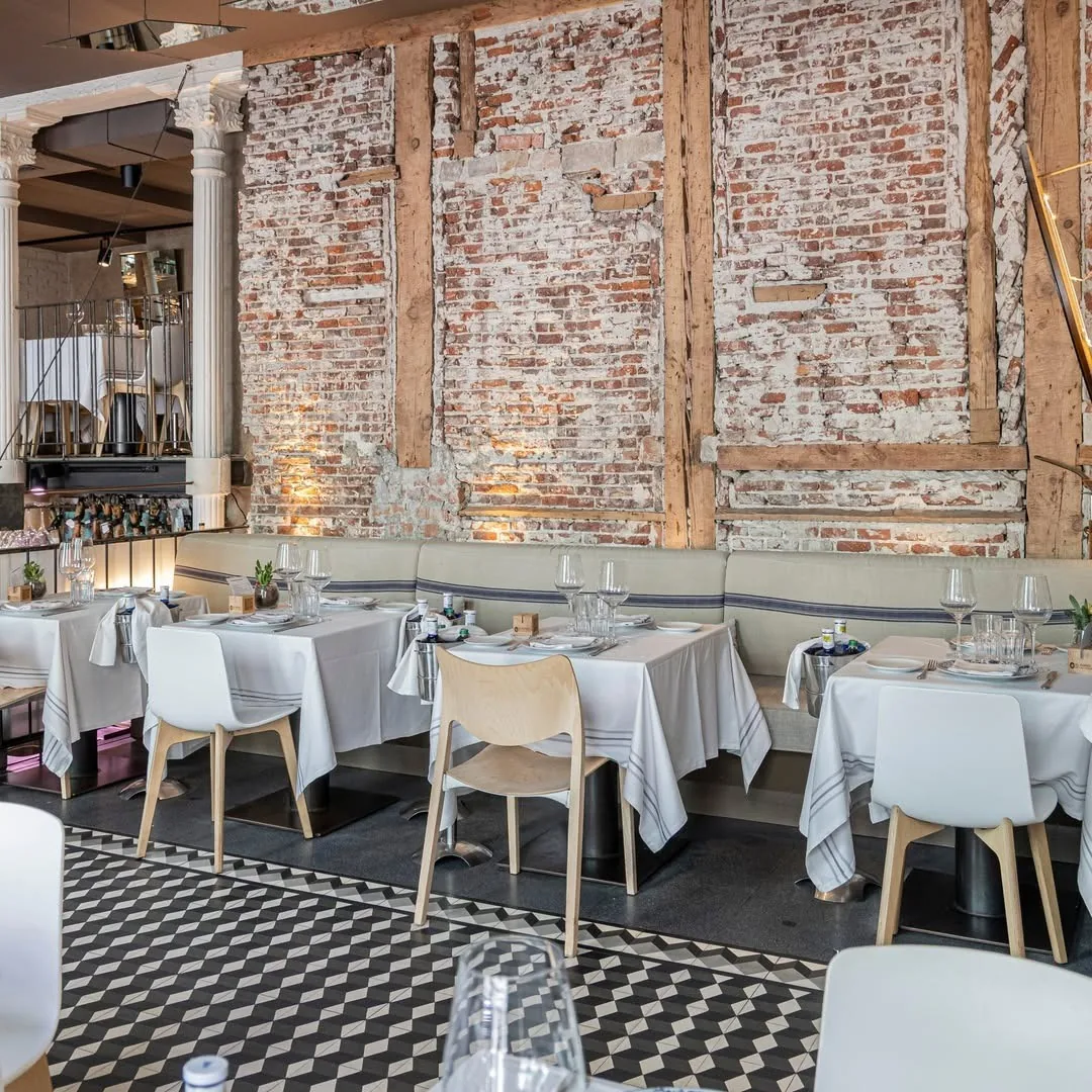 A dining room with white-clothed tables, brick walls and a chequered floor