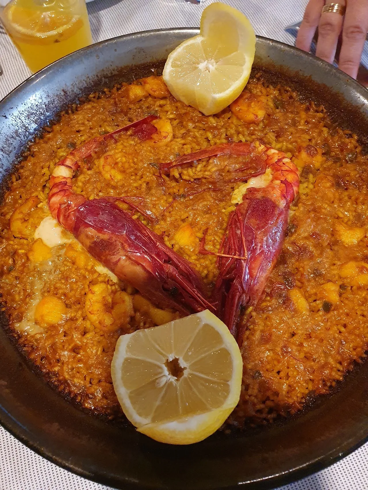 A paella pan of orange rice with a red prawn and a lemon half