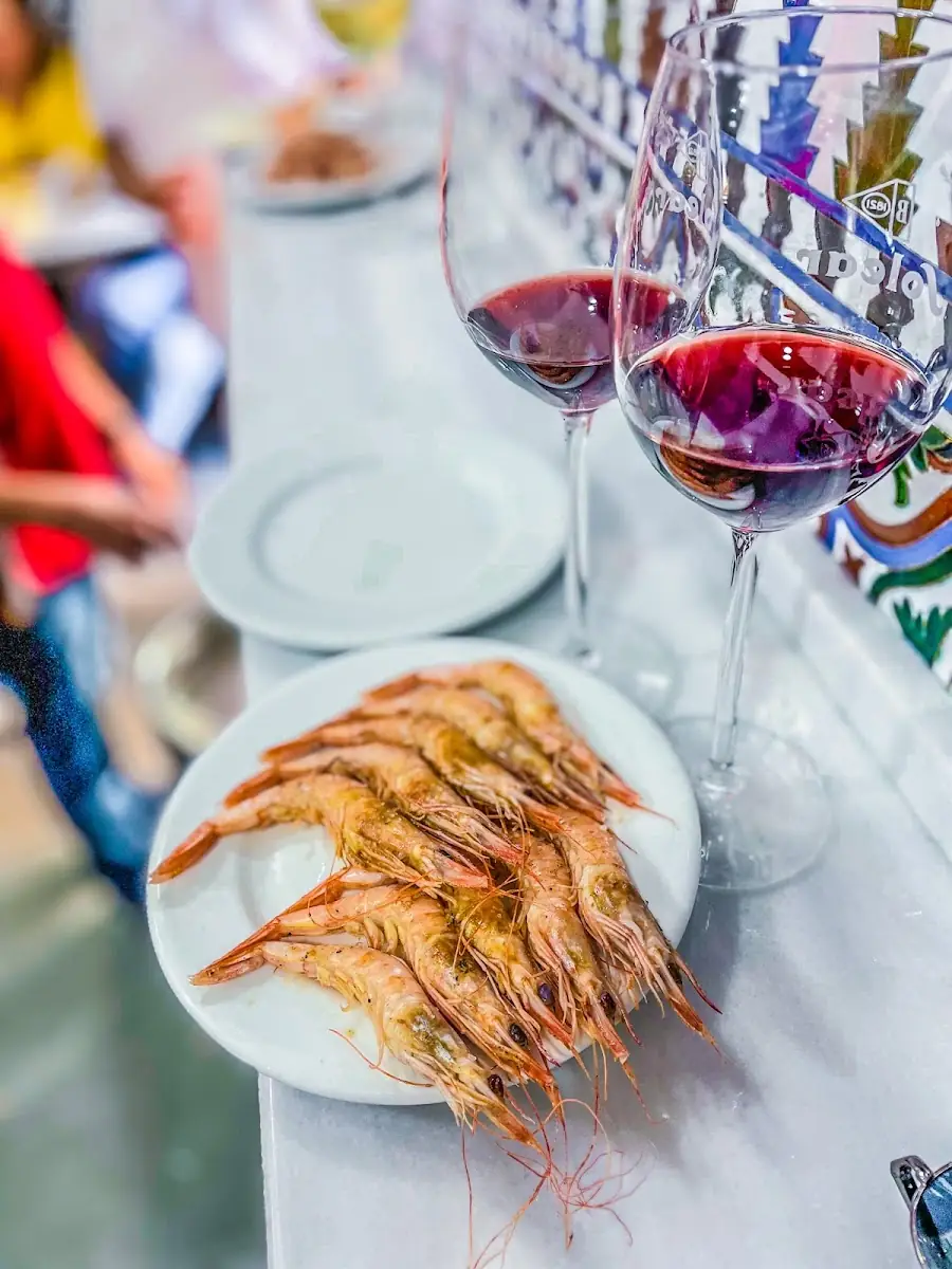 Plate of grilled prawns with two glasses of red wine on a marble bar top