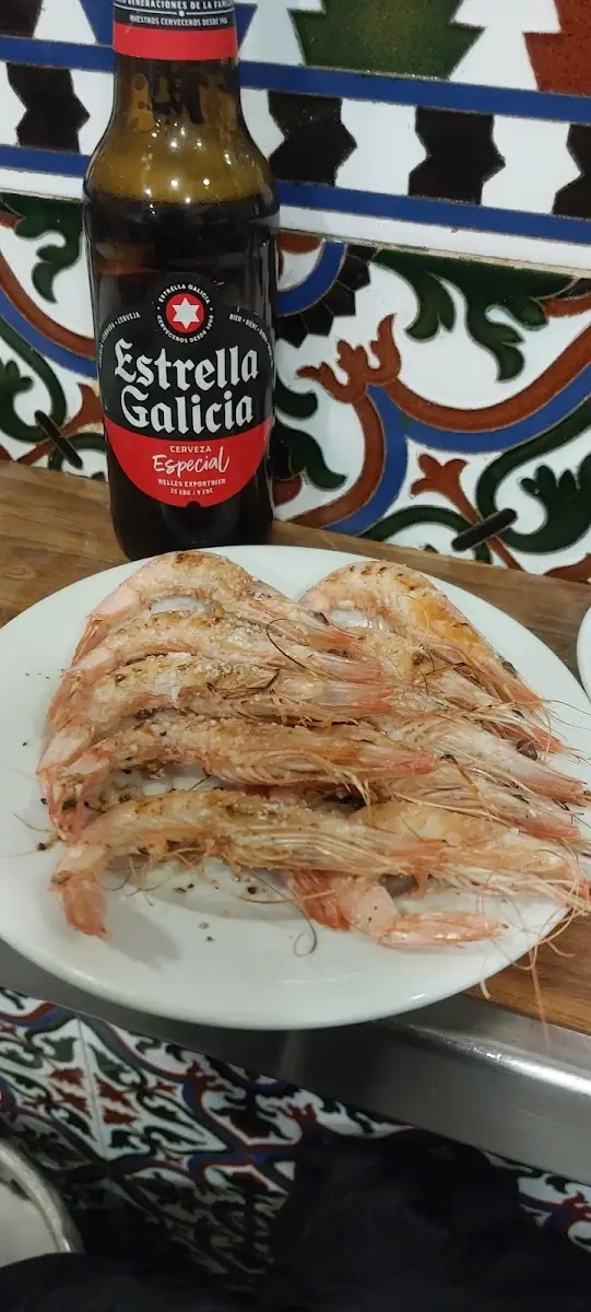 Plate of grilled prawns beside an Estrella Galicia beer bottle against a tiled wall
