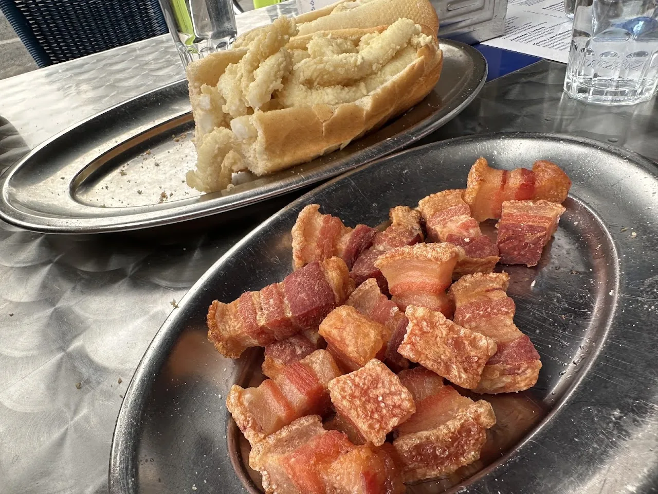A plate of cubed cured ham beside a fried calamari sandwich
