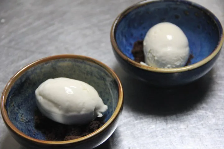 Two blue-glazed bowls, each holding a scoop of pale ice cream over dark crumble.