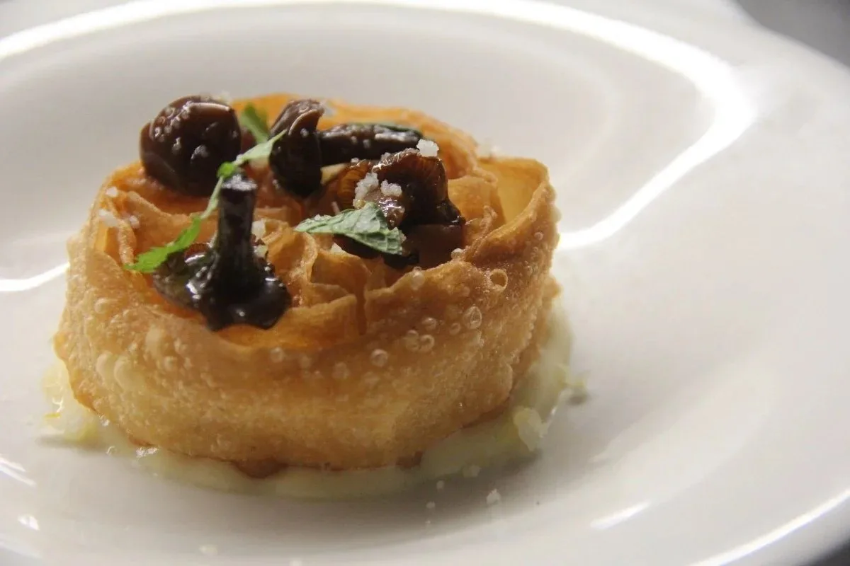 A golden pastry case topped with cooked mushrooms and herbs on a white plate