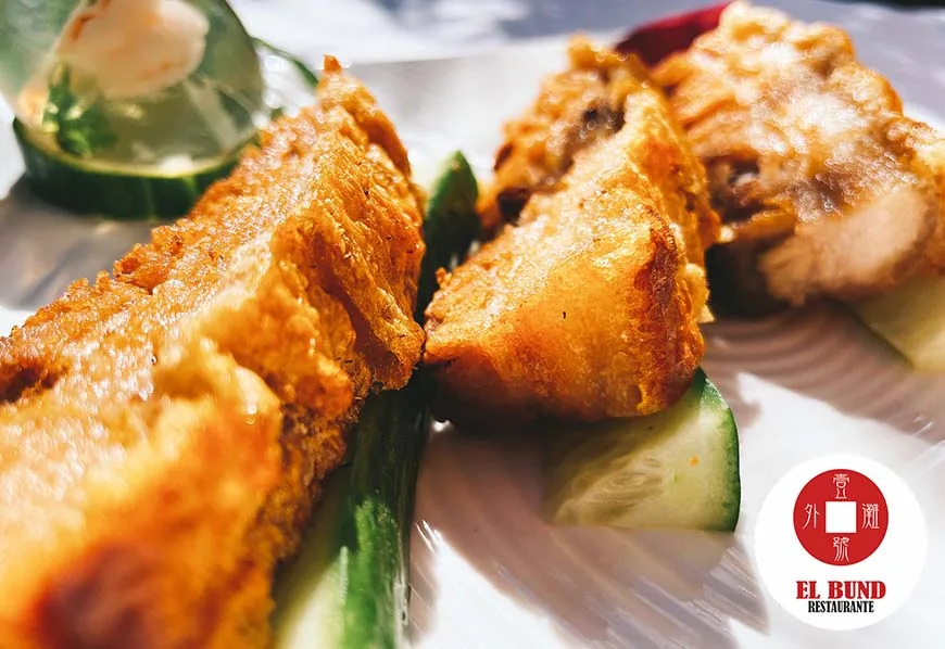 Pieces of golden battered fish on cucumber slices on a white plate in bright sunlight