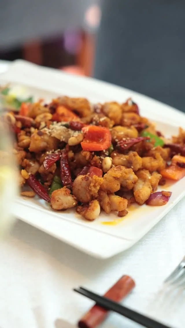Stir-fried chicken pieces with dried chilies on a white square plate with chopsticks