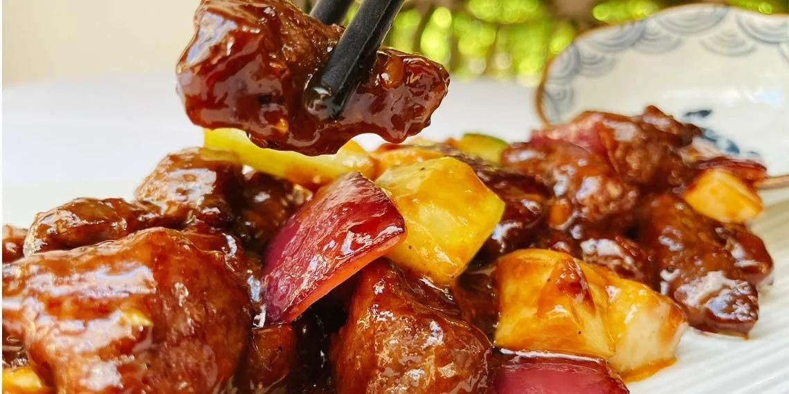 Glazed sweet and sour pork pieces with peppers on a white plate