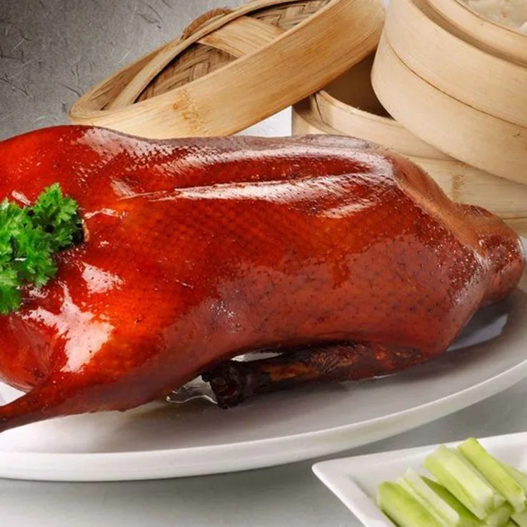 A whole glossy roast duck on a plate with bamboo steamers behind