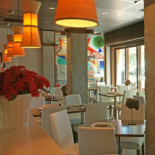 Dining room with orange fabric pendant lamps, a red poinsettia centerpiece, white chairs at wooden tables, and a colorful abstract mural on the far wall.