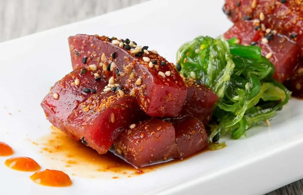 Marinated tuna cubes with sesame seeds and seaweed salad on a white plate