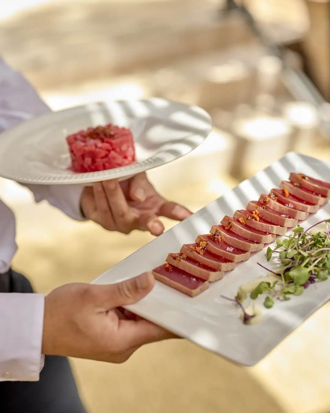 Waiter carrying a plate of tuna tartare and a tray of sliced seared tuna with microgreens