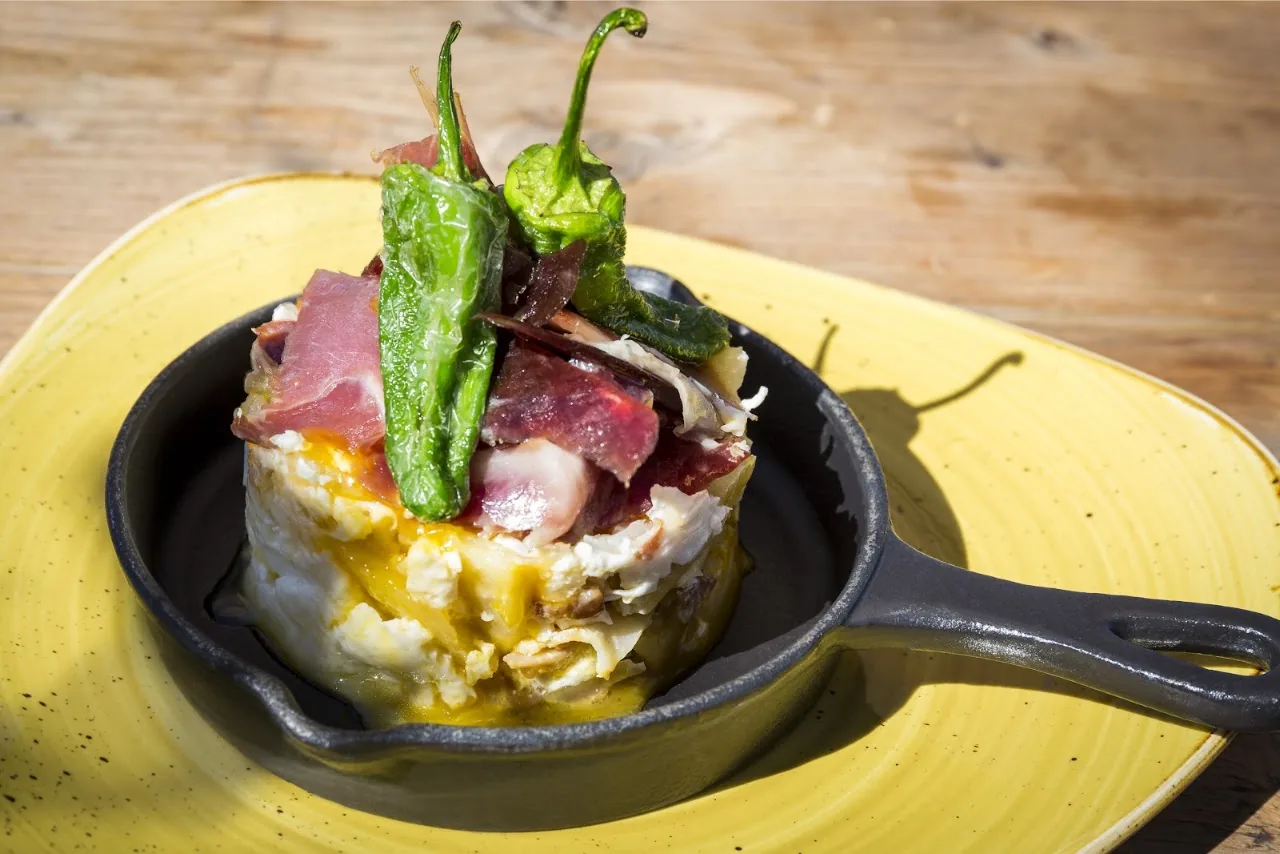 A small pan of padron peppers with cured ham and egg