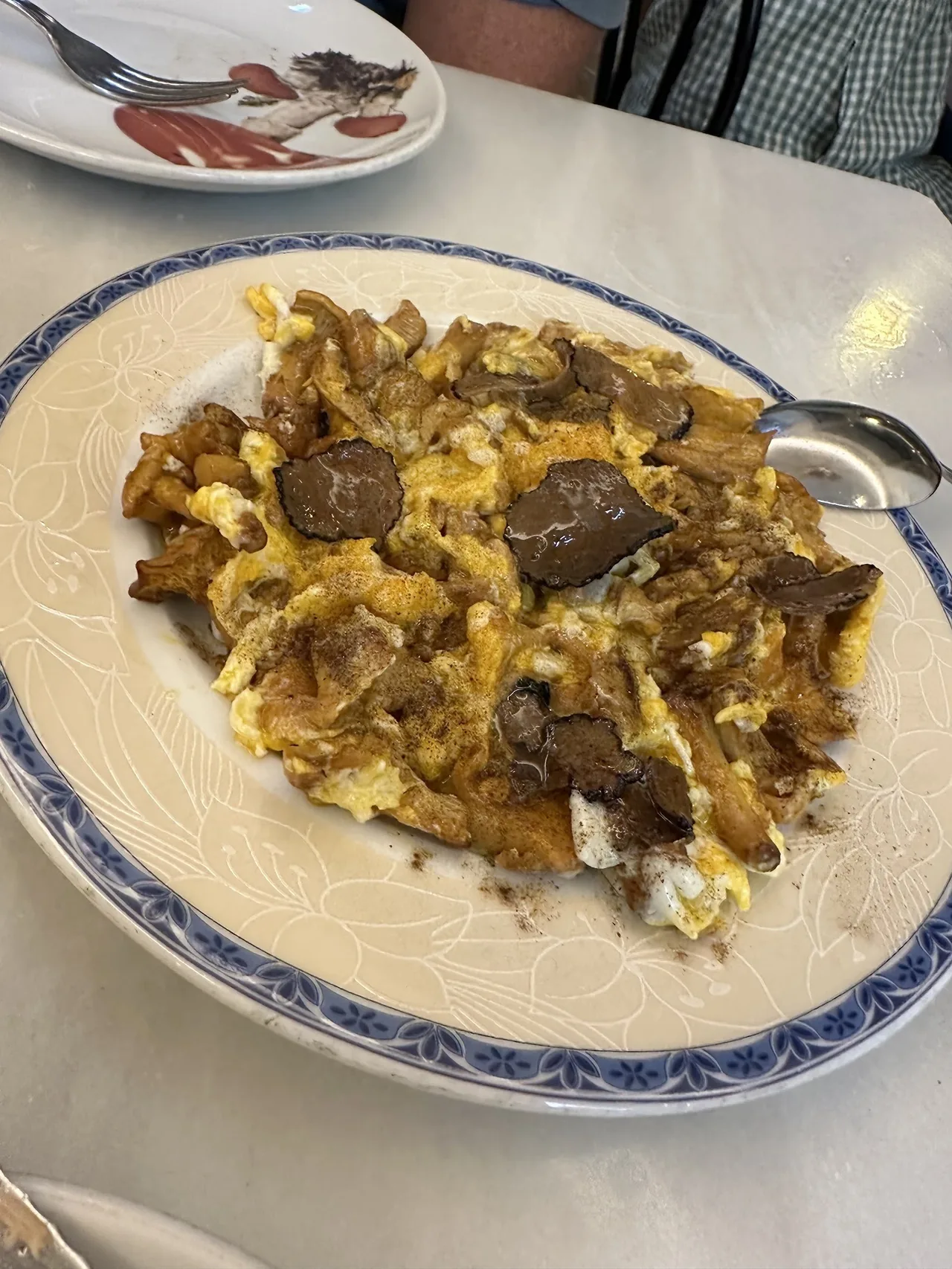 A plate of scrambled egg with mushrooms and shavings on a white plate