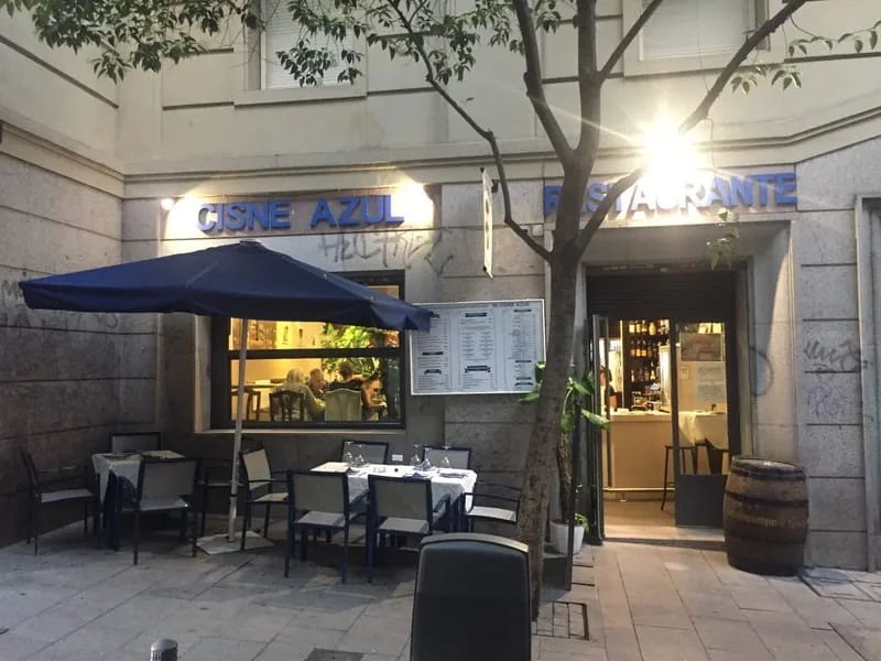 The street entrance of a restaurant with an awning and tables outside