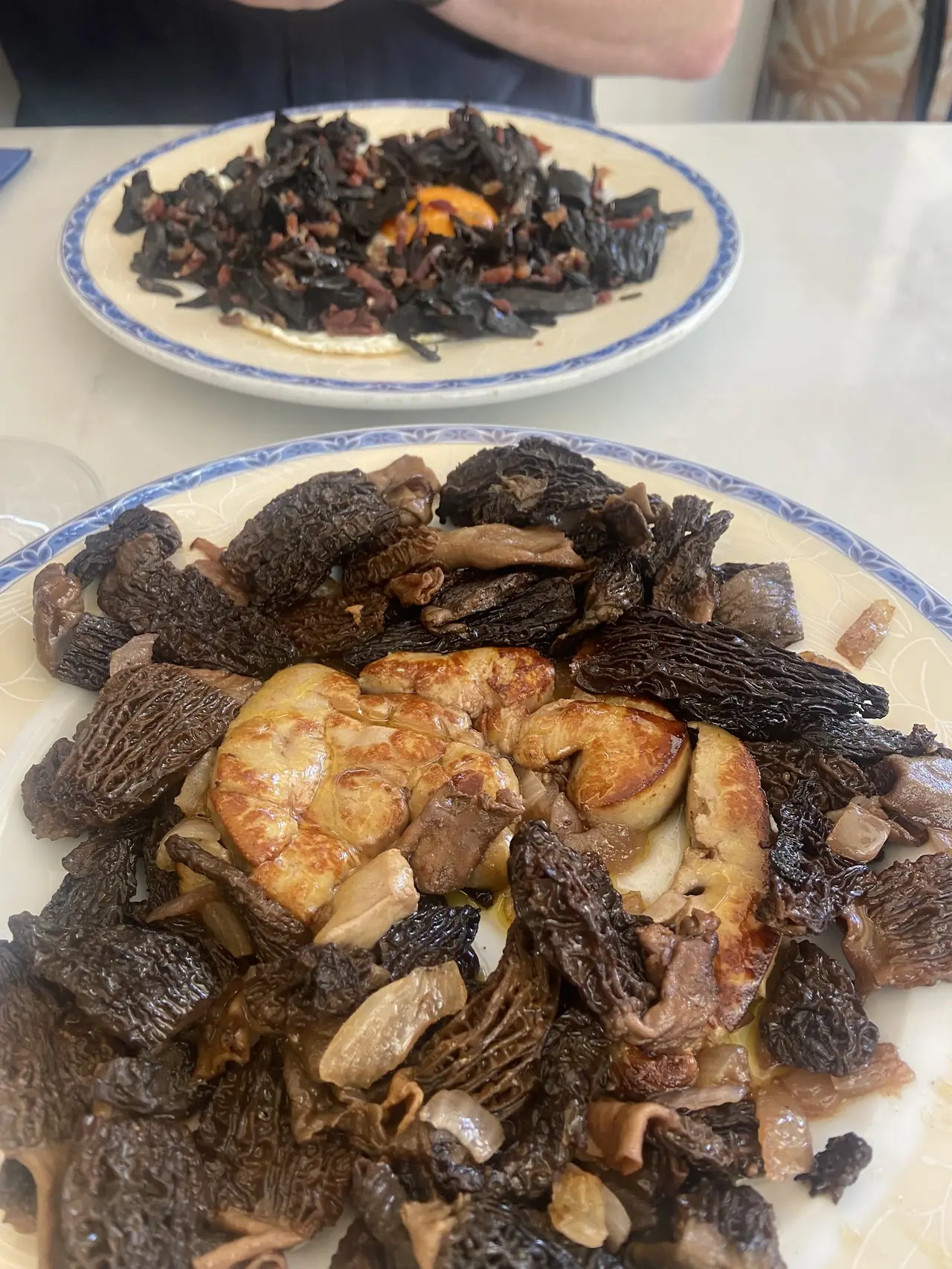 Seared foie gras with black morel mushrooms on a plate, another mushroom dish in the background