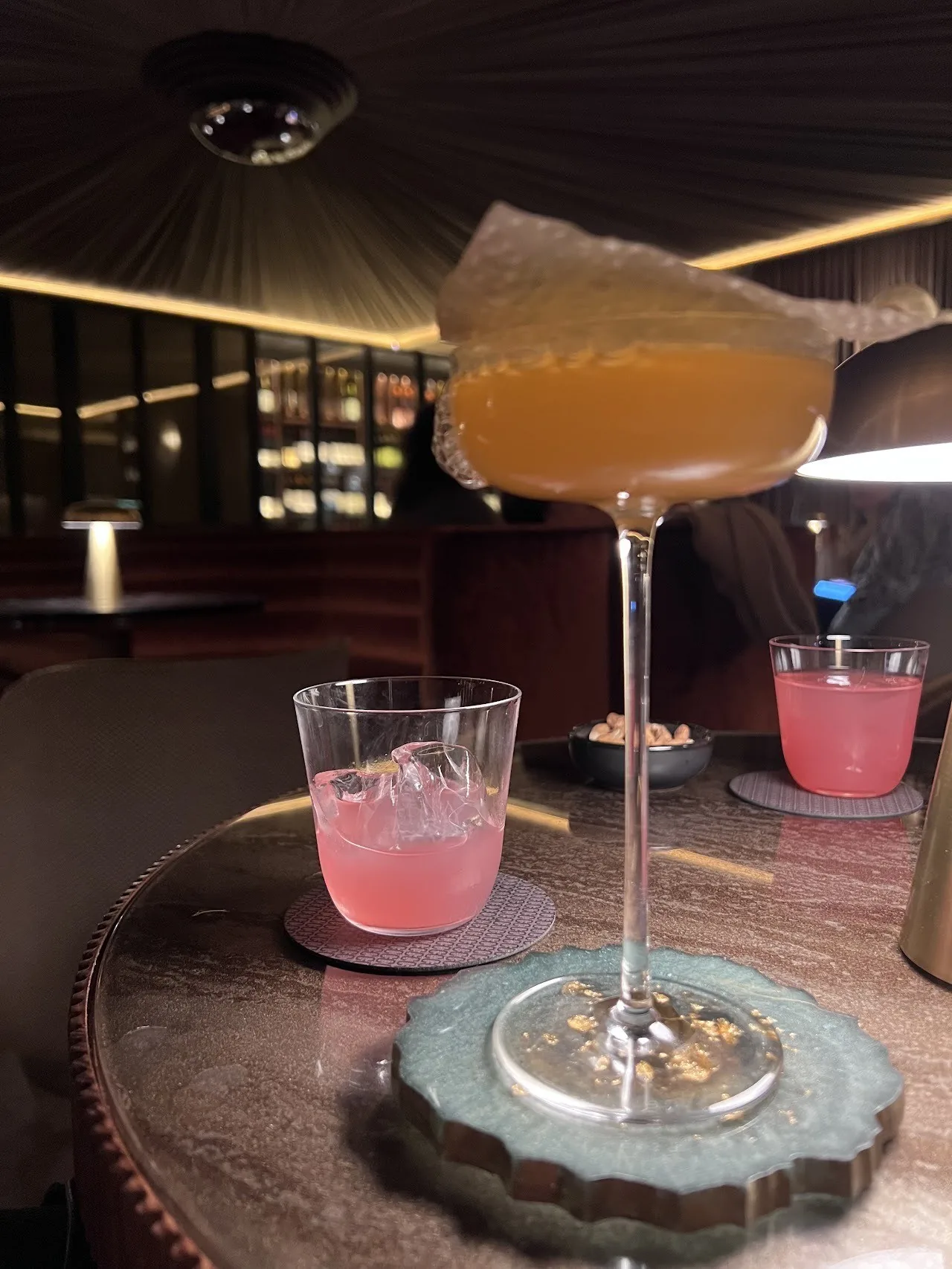A coupe cocktail and two pink drinks on a round table in a dim bar