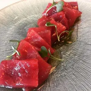 Row of thick-cut red tuna sashimi slices garnished with microgreens on a wood-grain plate