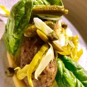 Meat croquette or tartare mound topped with pickled onion, capers and cornichons, wrapped in baby gem lettuce