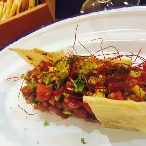 Tartare with avocado and tomato served in a folded toast shell, garnished with red chili threads on a white plate
