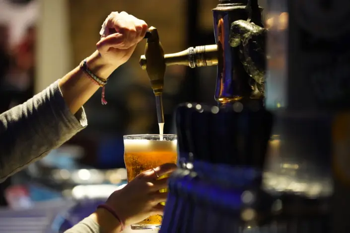 A hand pouring a glass of amber craft beer from a tap, El Drapaire de la Cervesa Artesana.