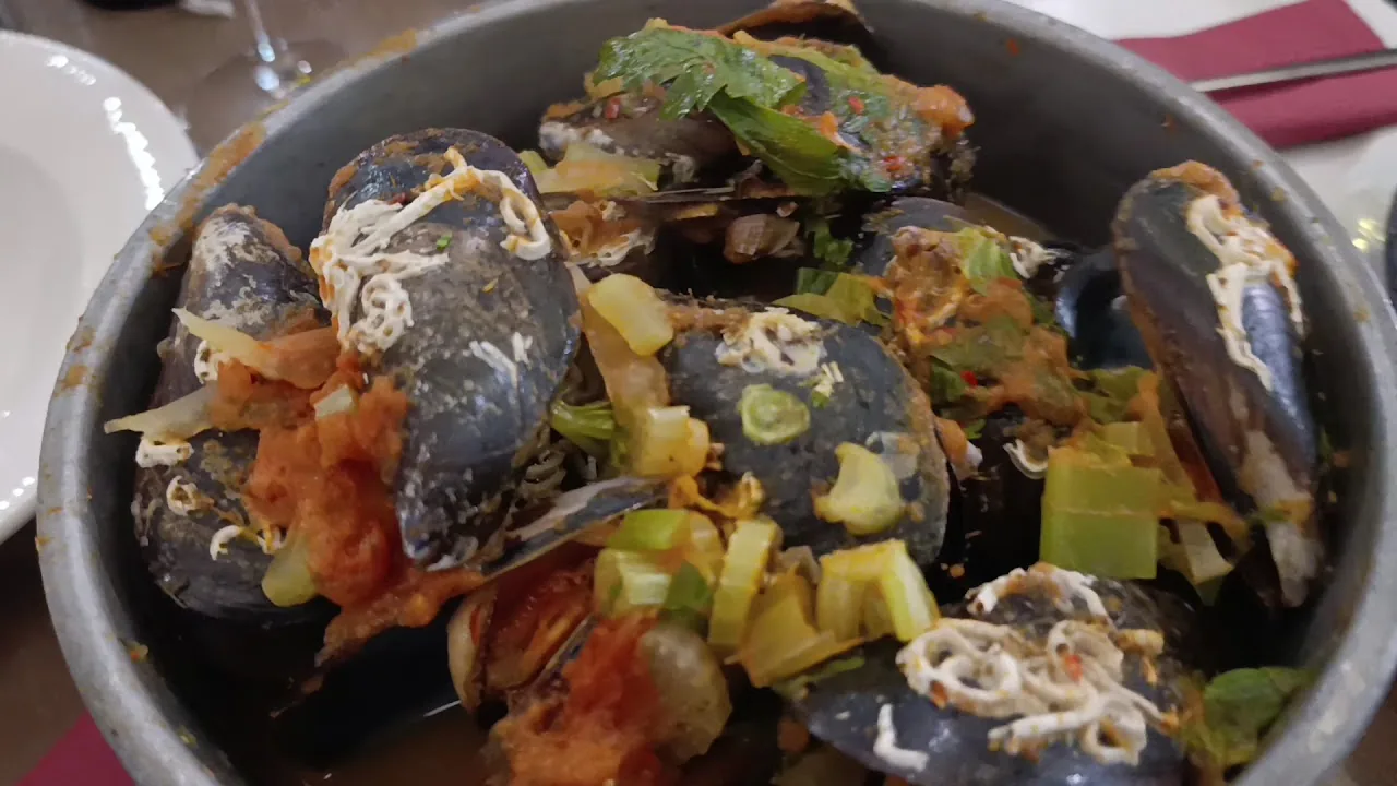 A pot of mussels with vegetables in sauce