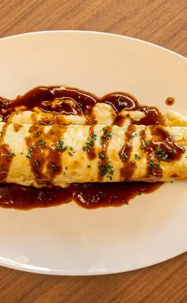 Rolled French-style omelette on a white plate drizzled with brown gravy and chopped chives