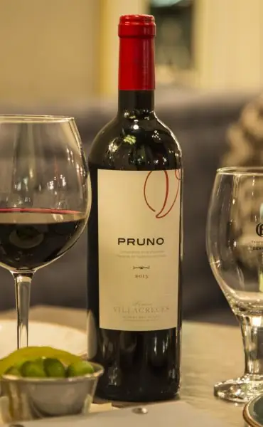 Bottle of Pruno red wine with a poured glass of red wine and a bowl of green olives on a table