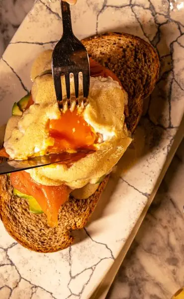 Poached egg on toast with smoked salmon and avocado, runny yolk cut open, on a marble plate