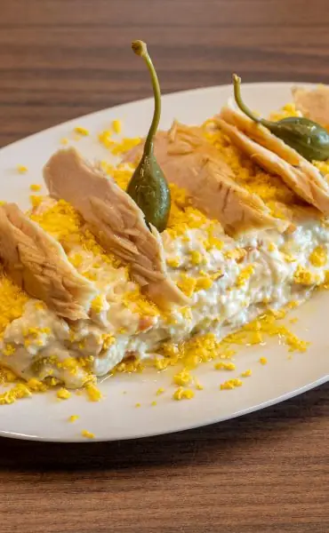 Ensaladilla rusa topped with flaked tuna, grated egg yolk and green caper berries on a white oval plate