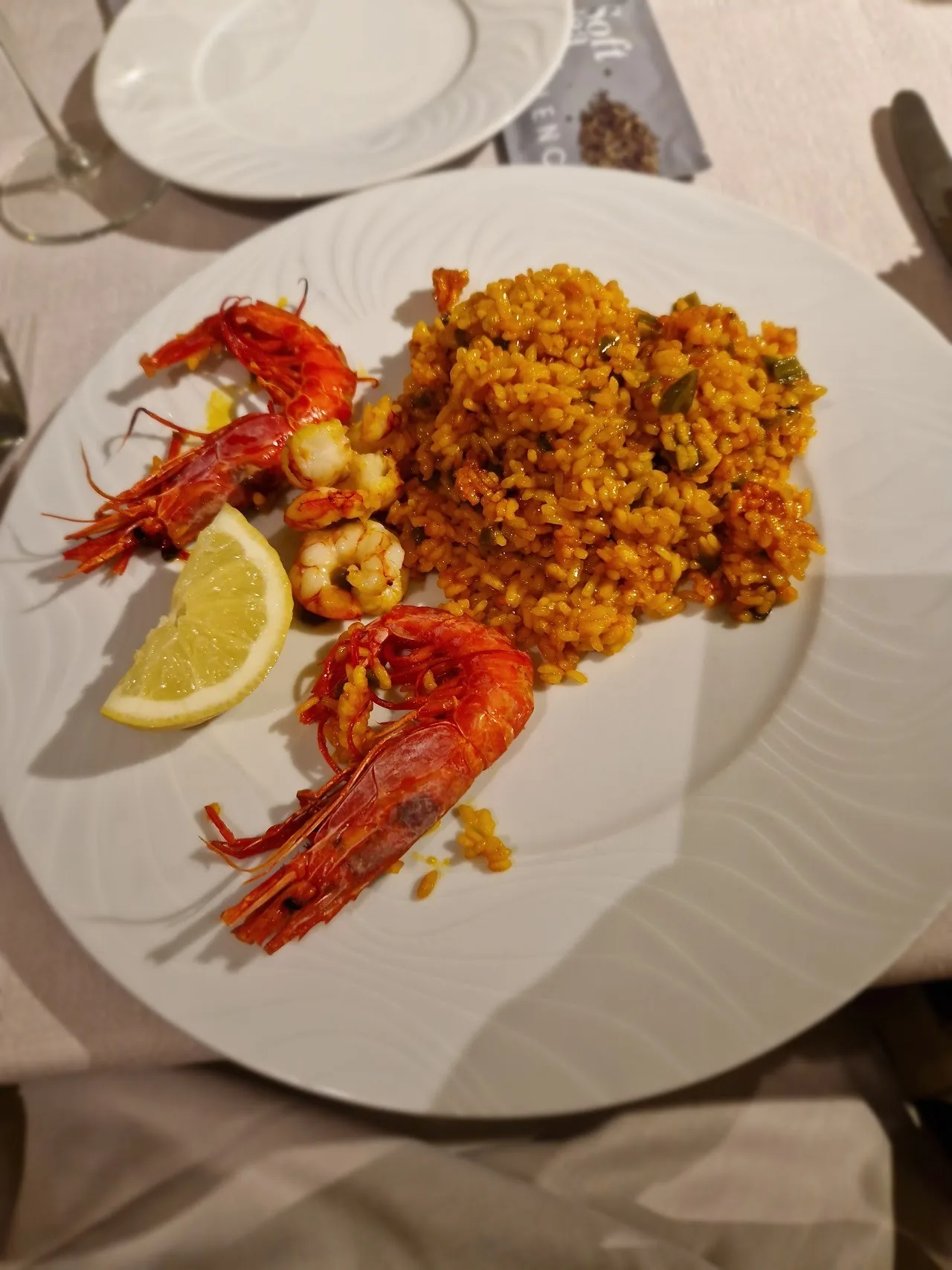 A white plate of orange rice with two red prawns and a lemon wedge