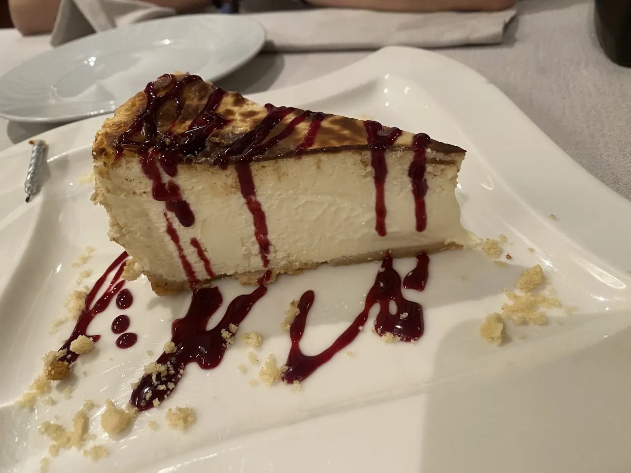 A slice of cheesecake drizzled with red berry sauce