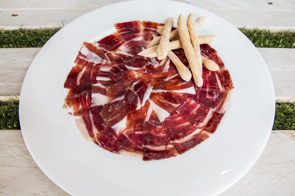 Thinly sliced cured ham fanned on a plate with breadsticks