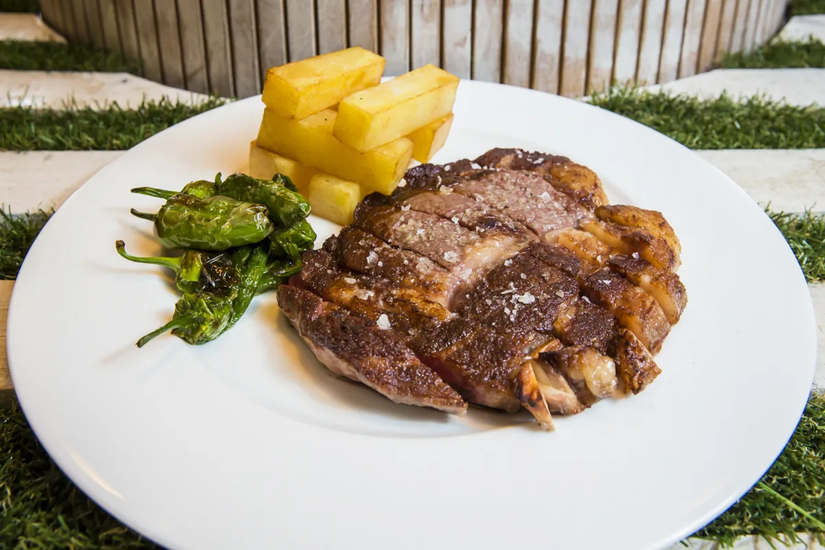 A grilled steak plate with pineapple chunks and padrón peppers