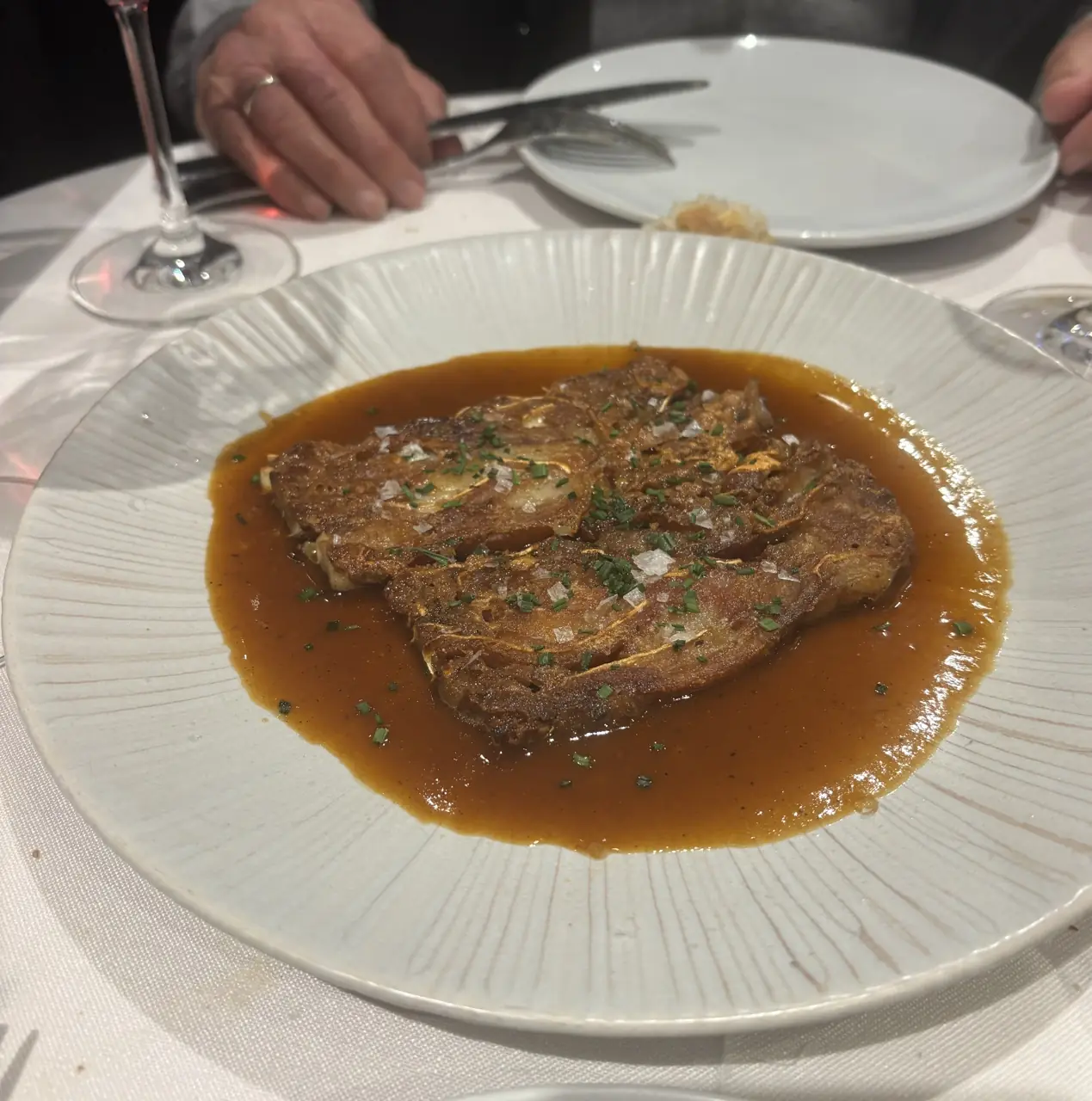 Seared meat slices in brown sauce garnished with chives and salt flakes on a textured plate